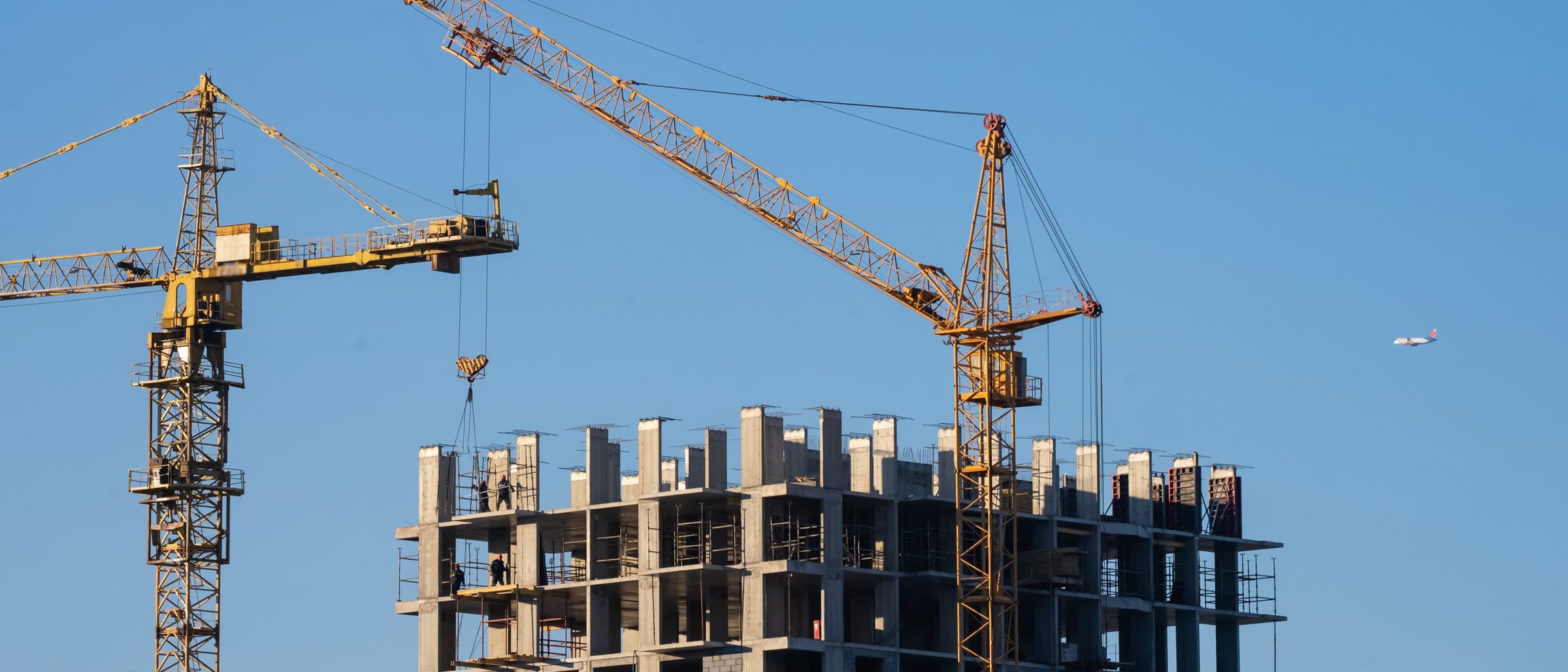 Tower cranes over a high rise building under construction against a blue sky