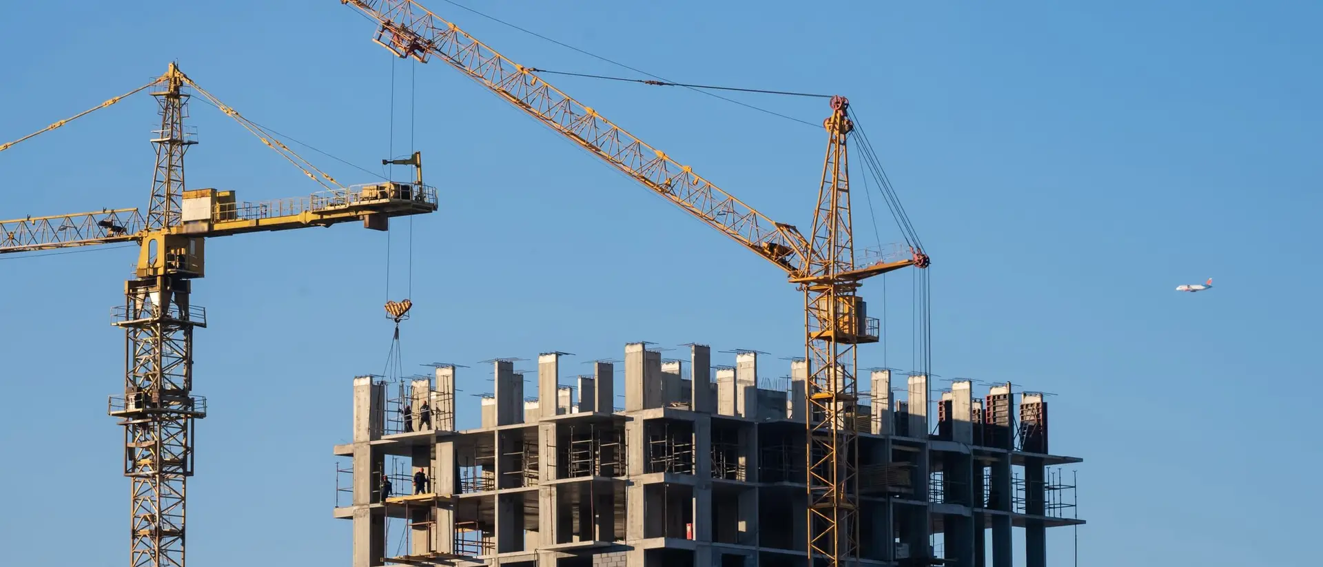 Tower cranes over a high rise building under construction against a blue sky