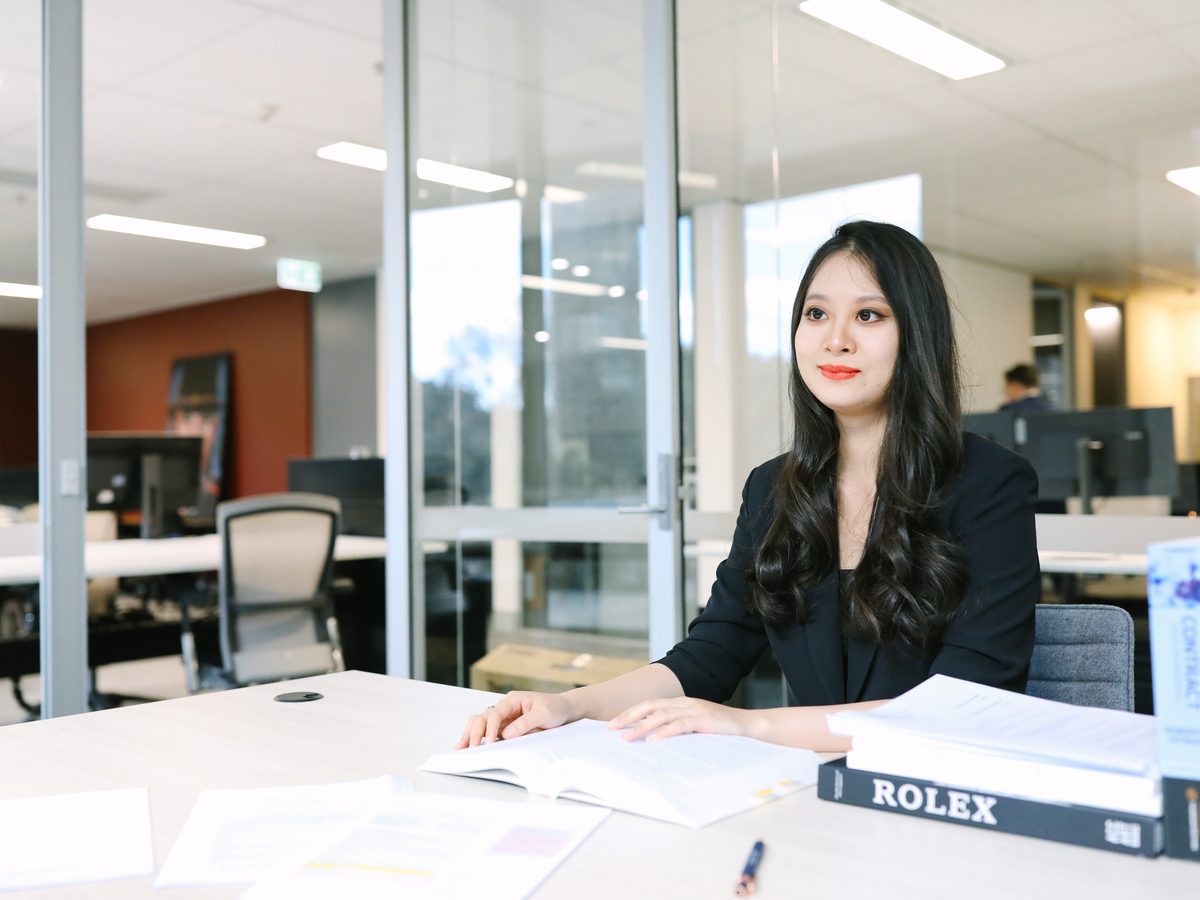 A junior lawyer at a desk with open contract texts and papers