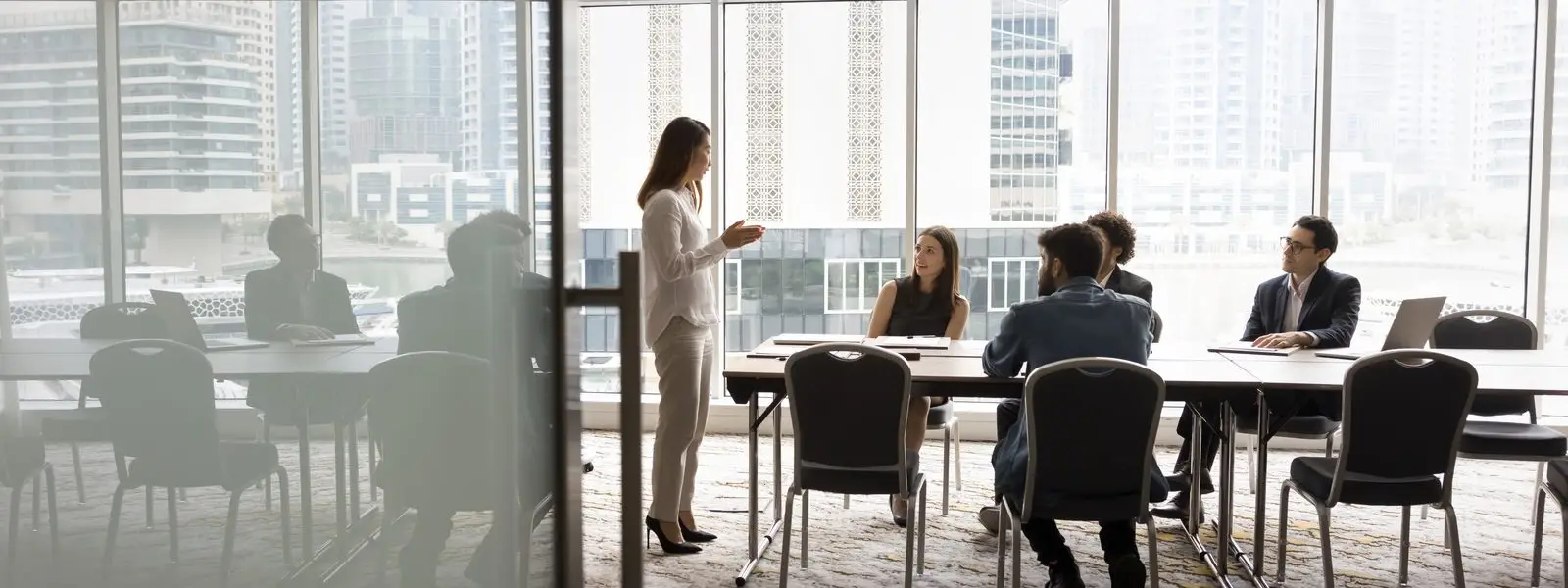 A meeting in a boardroom with a city view behind it