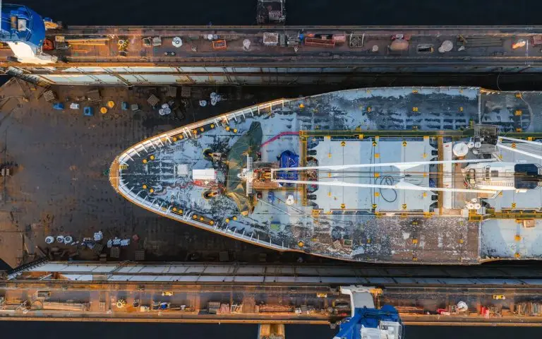 A vessel under work in a dry dock seen from directly above, with the dock walls and gantry cranes either side