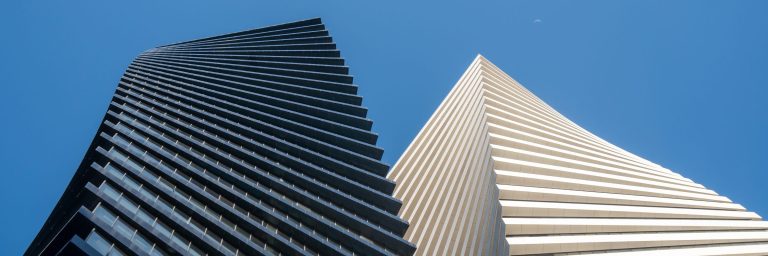 Two towers rising side by side, one dark and one pale, seen from below against a clear sky