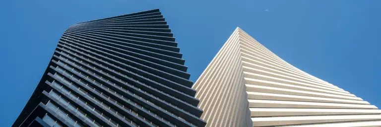 Two towers rising side by side, one dark and one pale, seen from below against a clear sky