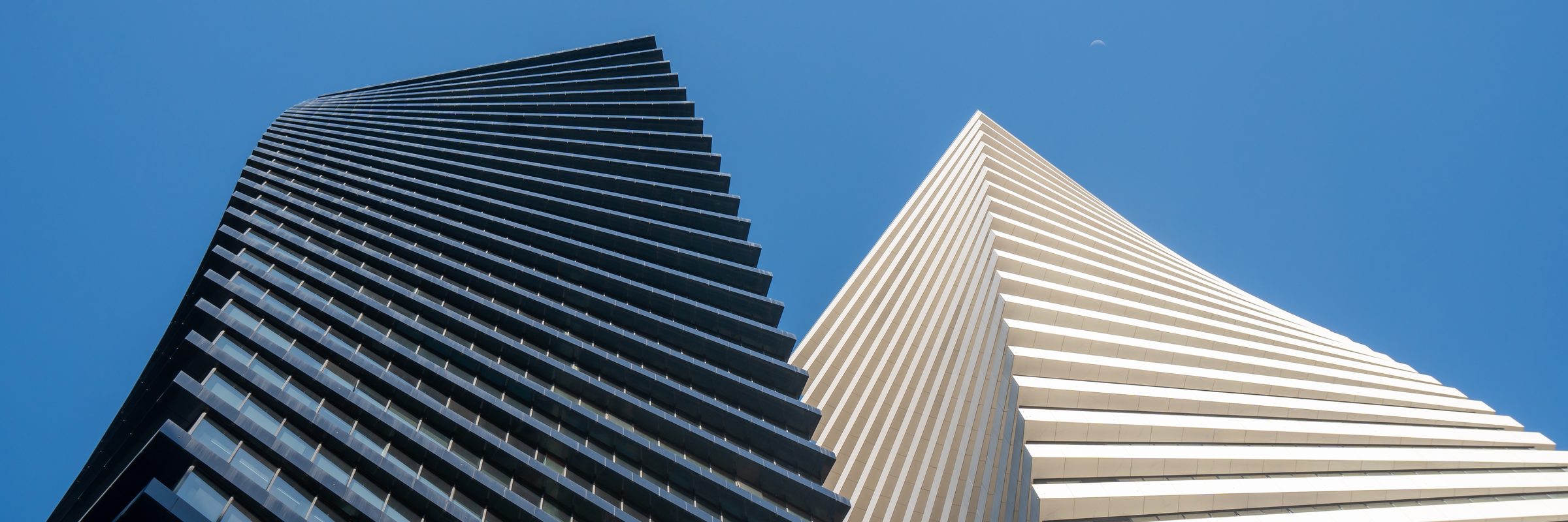 Two towers rising side by side, one dark and one pale, seen from below against a clear sky