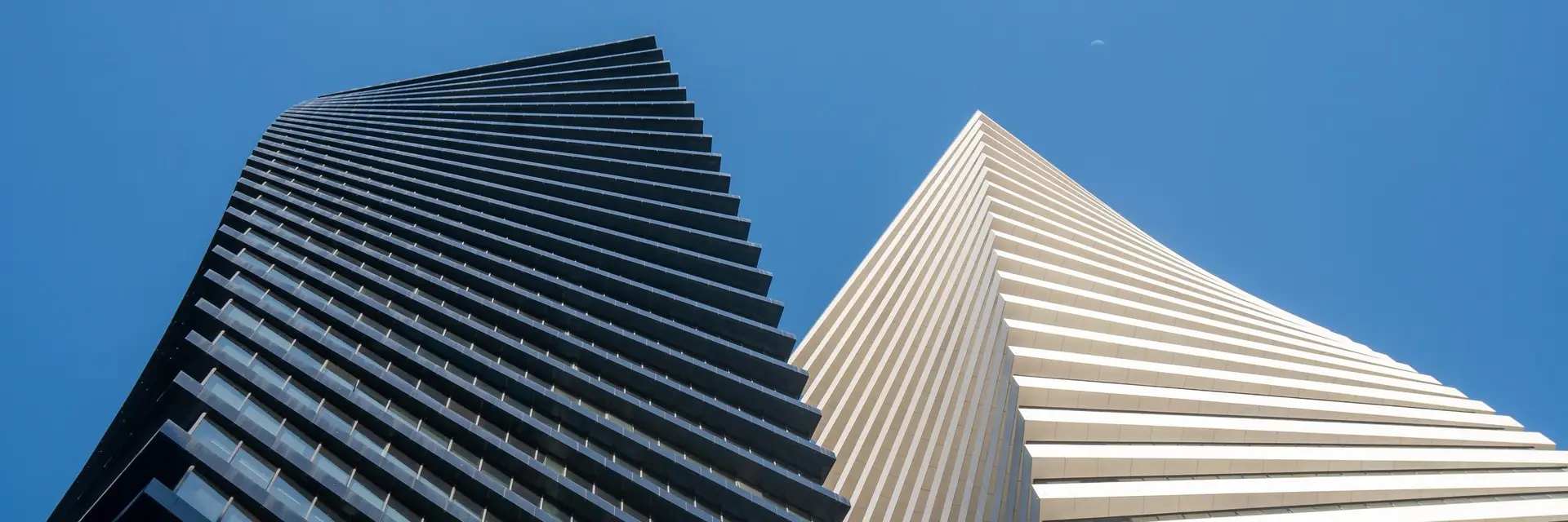 Two towers rising side by side, one dark and one pale, seen from below against a clear sky