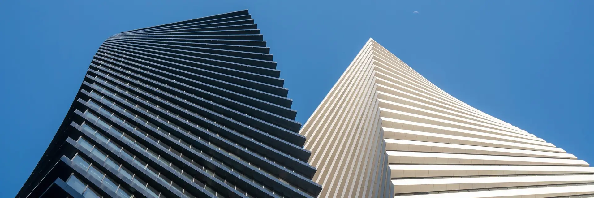 Twin tower facades seen from below against a blue sky