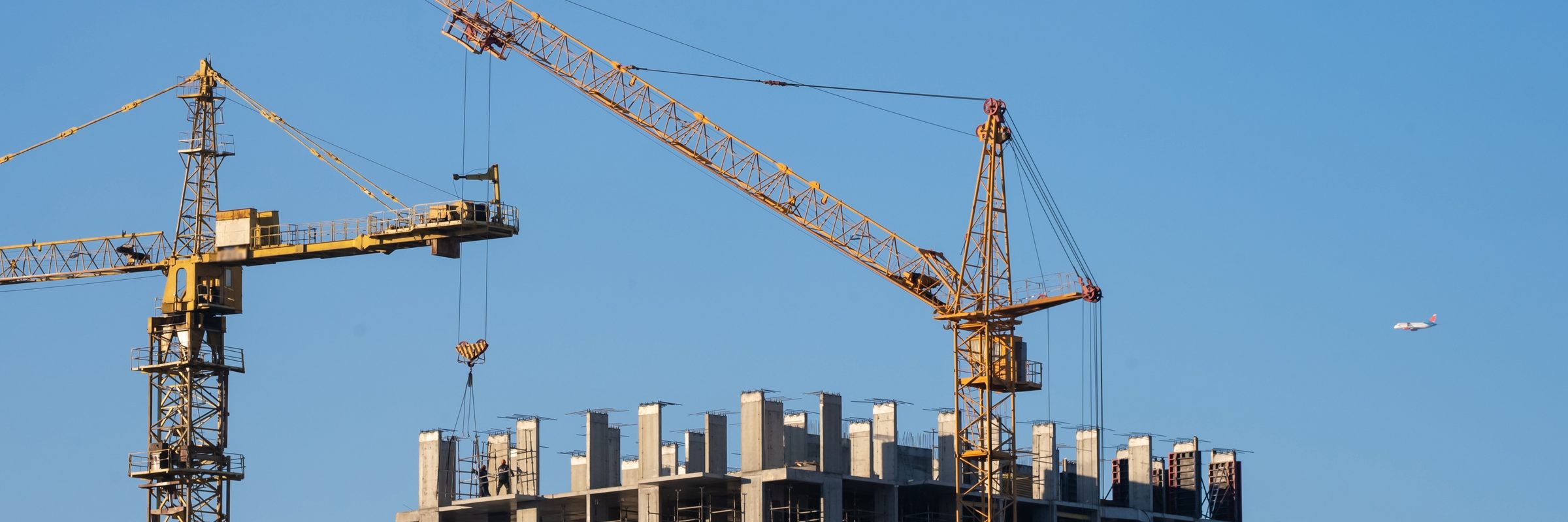 Two tower cranes over the concrete frame of a high-rise building under construction